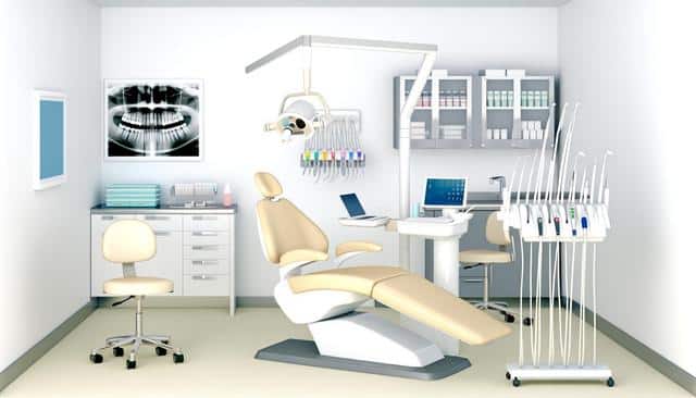 A modern dental office with a beige dental chair, tools, computer, and X-ray image on the wall.