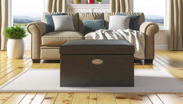 A cozy living room with a brown sofa, blue and white pillows, a dark ottoman, and large windows.