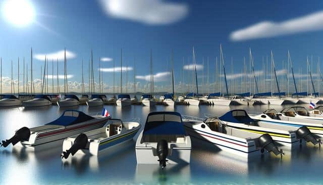 A sunny marina scene with several motorboats and sailboats docked on calm water.