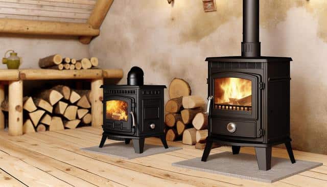 Two wood-burning stoves with burning fires, surrounded by stacked logs in a cozy room.