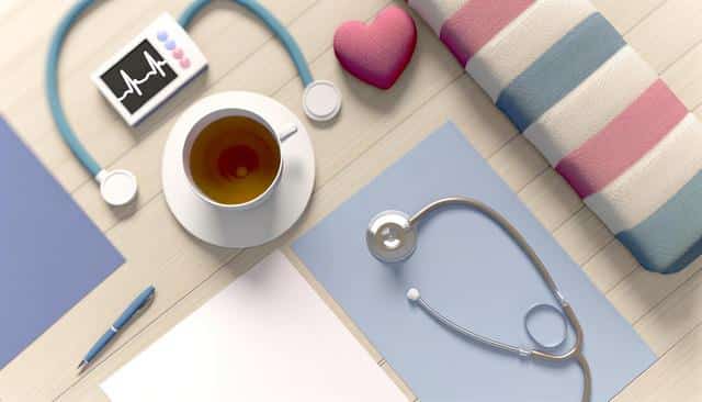 A stethoscope, tea cup, striped cushion, pink heart, pen, and ECG monitor on a wooden surface.