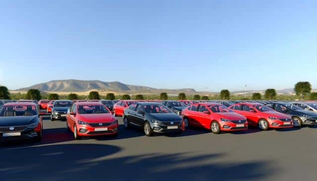 A large group of red and black cars parked in an open lot with mountains in the background under a clear blue sky.