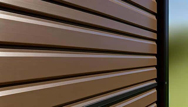 Close-up of brown corrugated metal siding with vertical lines and a blurred green background.