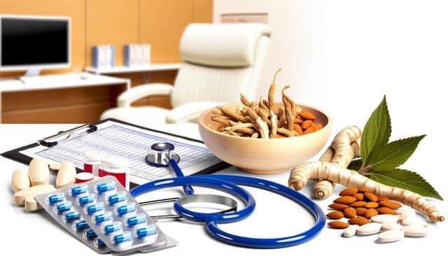 Medical office backdrop with pills, stethoscope, clipboard, ginseng root, almonds, and leaves in the foreground.