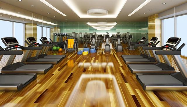 A modern gym with treadmills, exercise bikes, and balance balls on a wooden floor.