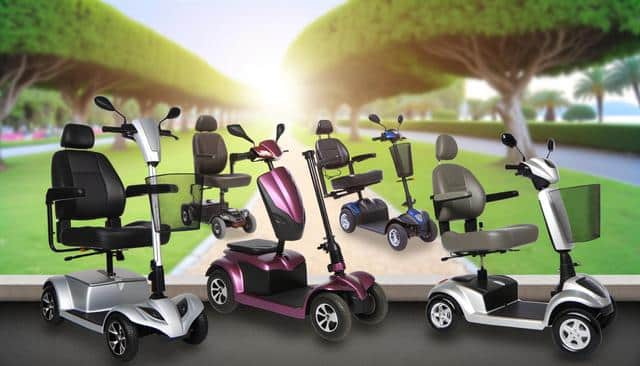 A group of five mobility scooters in various colors displayed on a smooth surface with a blurred park background.