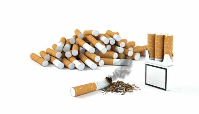 A pile of cigarettes, one lit and burning, with a cigarette pack nearby.