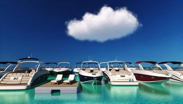 Multiple motorboats docked on turquoise water under a clear blue sky with a single fluffy cloud.