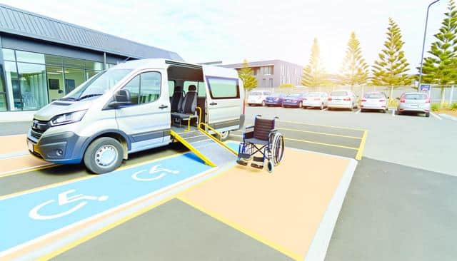 Accessible van with ramp deployed in parking lot; wheelchair nearby.